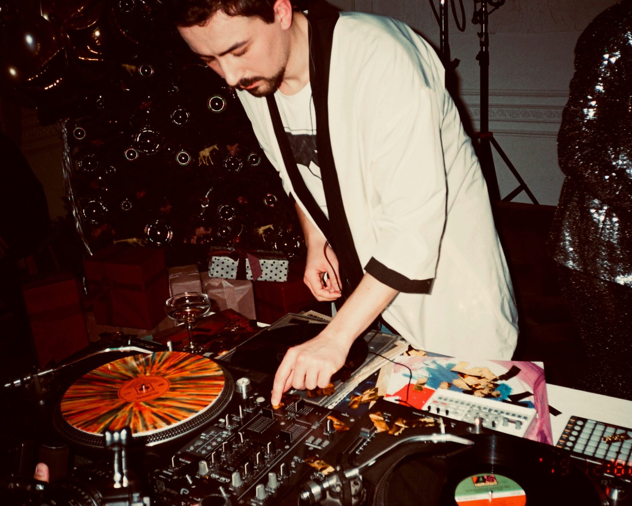 A DJ mixing records at a lively indoor party, surrounded by festive decorations.